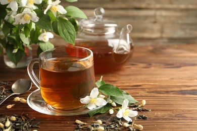 Photo of Aromatic jasmine tea in glass cup, teapot, brew and flowers on wooden table, closeup. Space for text