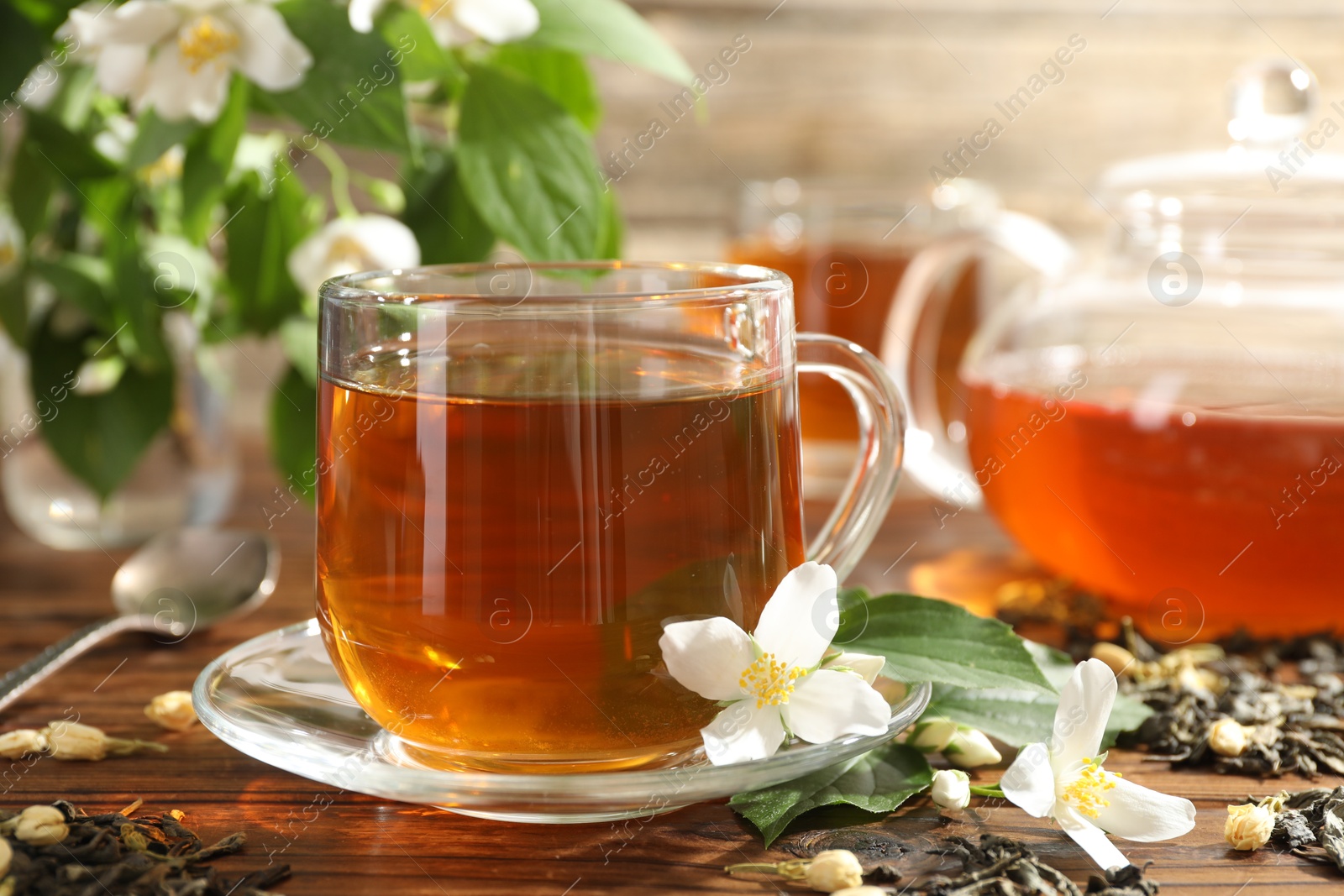 Aromatic jasmine tea in glass cup, teapot, brew and flowers on wooden table, closeup Photo of Aromatic jasmine tea in glass cup, teapot, brew and flowers on wooden table, closeup