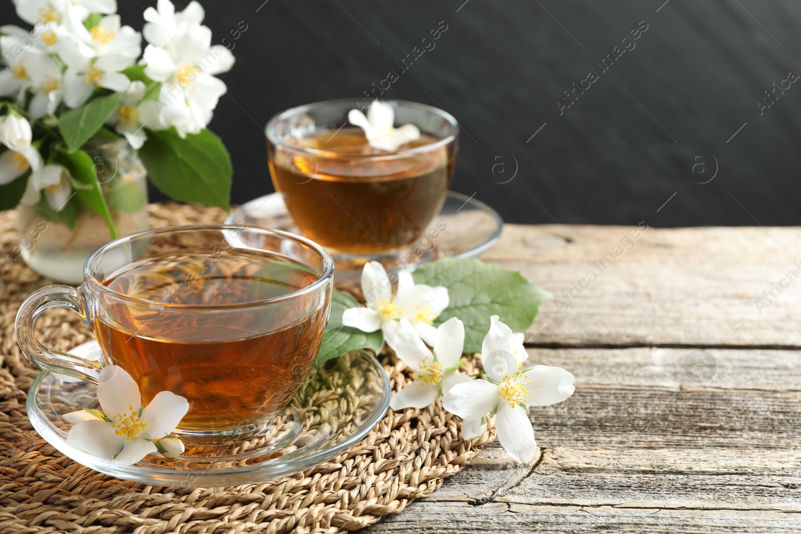 Aromatic jasmine tea in glass cups, flowers and green leaves on wooden table, closeup. Space for text Photo of Aromatic jasmine tea in glass cups, flowers and green leaves on wooden table, closeup. Space for text