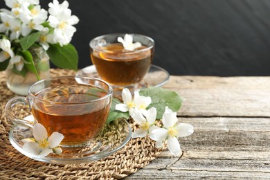 Photo of Aromatic jasmine tea in glass cups, flowers and green leaves on wooden table, closeup. Space for text