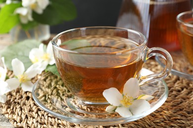 Photo of Aromatic jasmine tea in glass cup and flowers on table, closeup