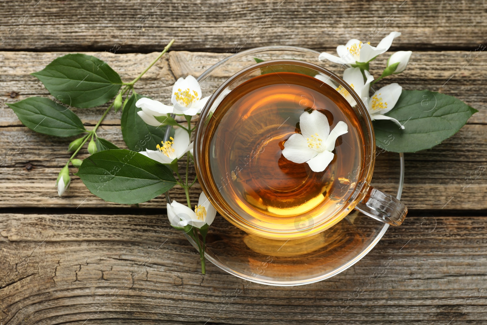 Aromatic jasmine tea in glass cup, flowers and green leaves on wooden table, flat lay Photo of Aromatic jasmine tea in glass cup, flowers and green leaves on wooden table, flat lay