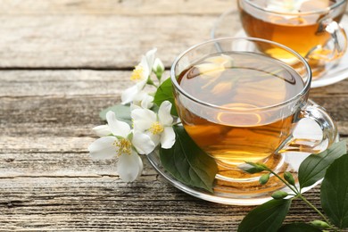 Photo of Aromatic jasmine tea in glass cups, flowers and green leaves on wooden table, closeup. Space for text