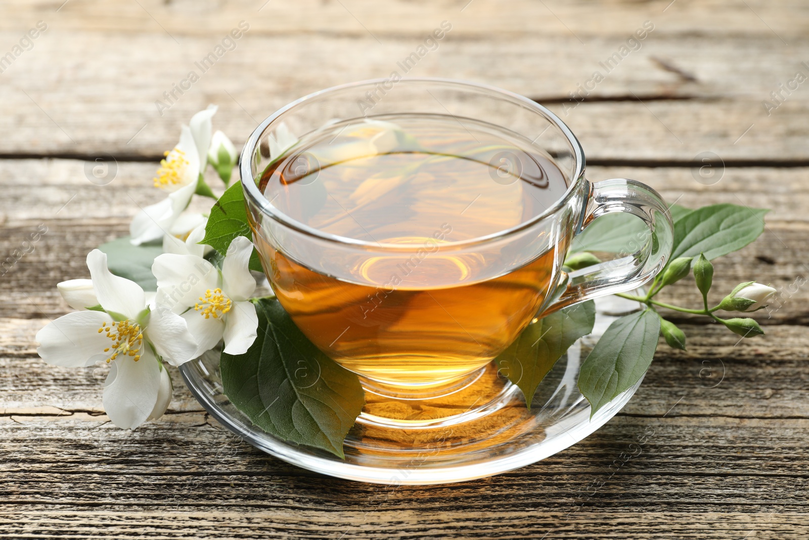 Aromatic jasmine tea in glass cup, flowers and green leaves on wooden table, closeup Photo of Aromatic jasmine tea in glass cup, flowers and green leaves on wooden table, closeup