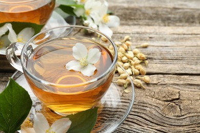 Photo of Aromatic jasmine tea in glass cups, brew and flowers on wooden table, closeup. Space for text