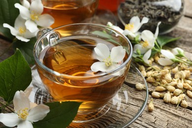 Photo of Aromatic jasmine tea in glass cups, brew and flowers on wooden table, closeup
