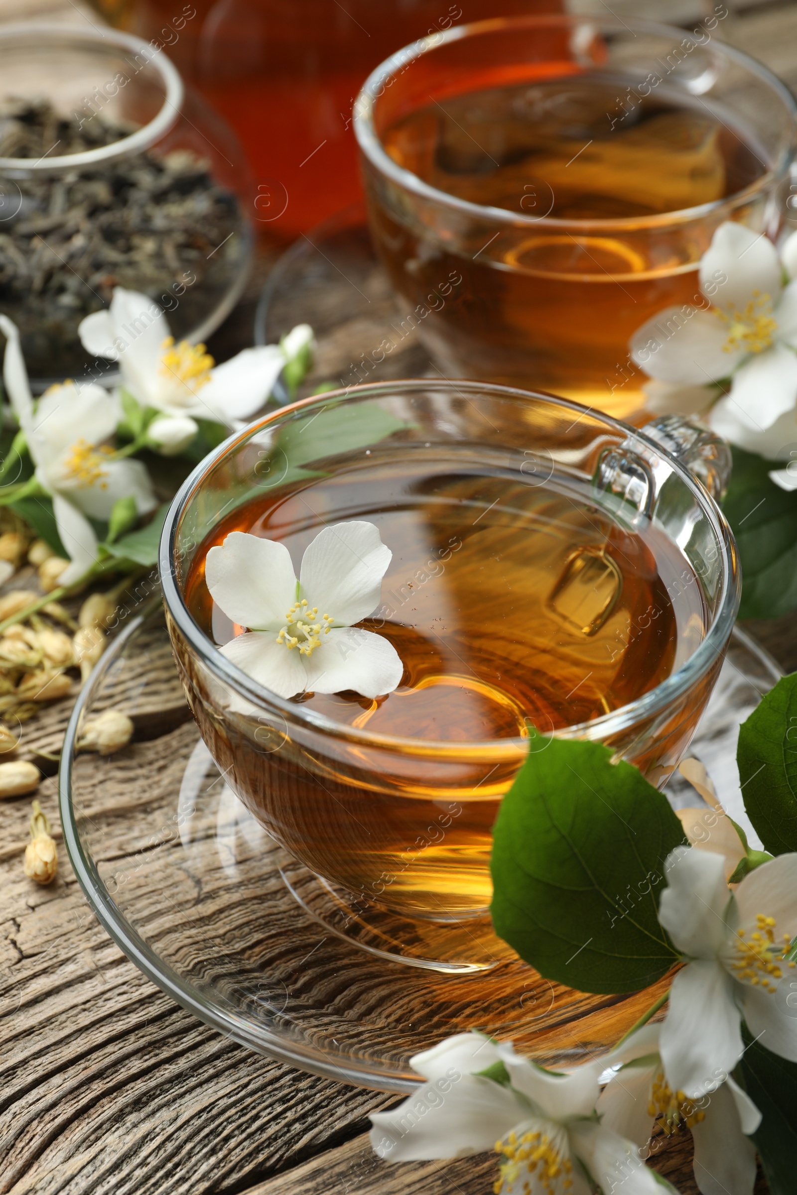 Aromatic jasmine tea in glass cups, brew and flowers on wooden table, closeup Photo of Aromatic jasmine tea in glass cups, brew and flowers on wooden table, closeup