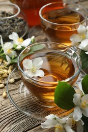 Photo of Aromatic jasmine tea in glass cups, brew and flowers on wooden table, closeup