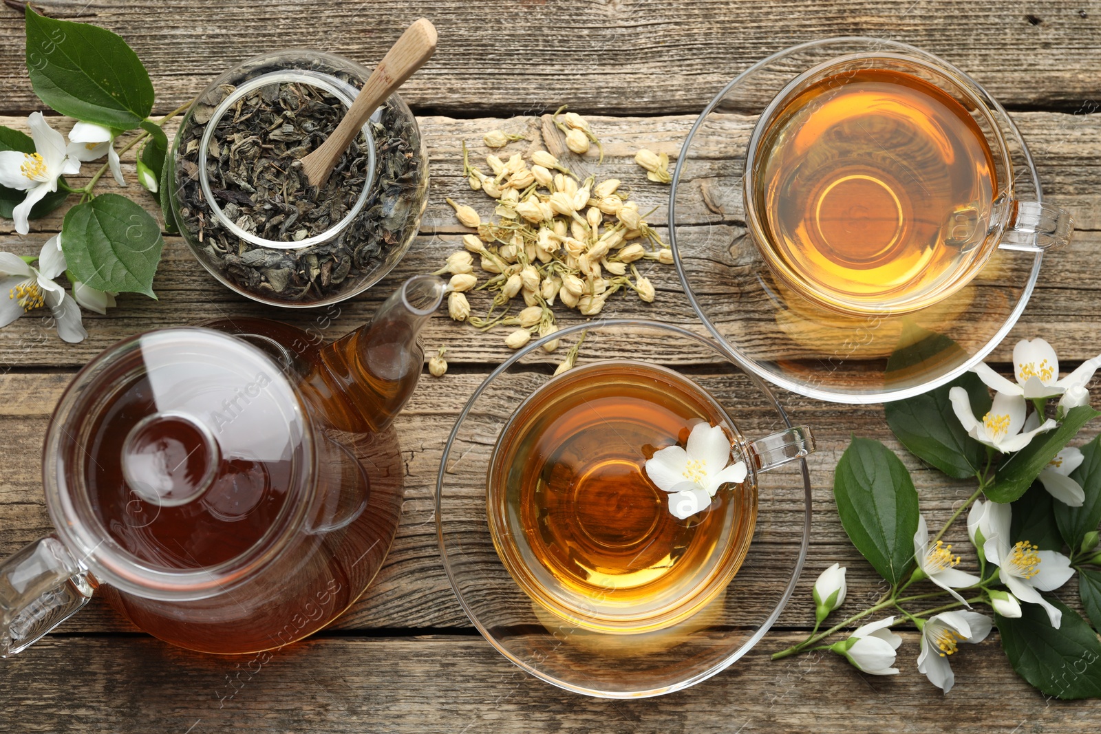 Aromatic jasmine tea in glass cups, teapot, brew and flowers on wooden table, flat lay Photo of Aromatic jasmine tea in glass cups, teapot, brew and flowers on wooden table, flat lay