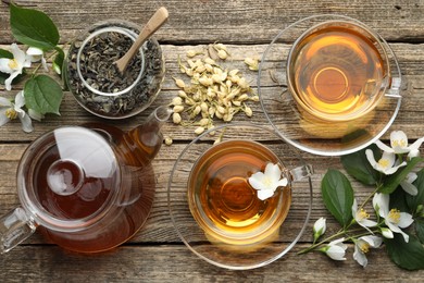 Photo of Aromatic jasmine tea in glass cups, teapot, brew and flowers on wooden table, flat lay