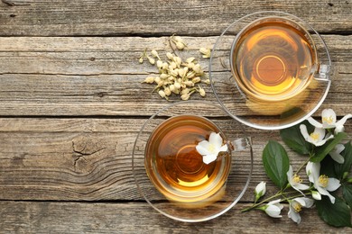 Photo of Aromatic jasmine tea in glass cups, flowers and green leaves on wooden table, flat lay. Space for text