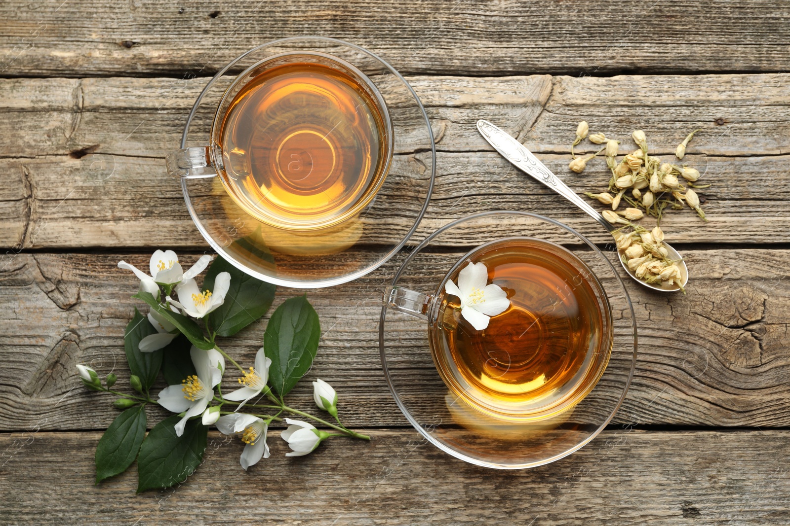 Aromatic jasmine tea in glass cups, flowers and green leaves on wooden table, flat lay Photo of Aromatic jasmine tea in glass cups, flowers and green leaves on wooden table, flat lay