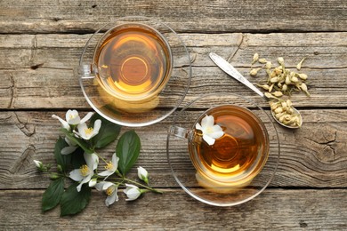 Photo of Aromatic jasmine tea in glass cups, flowers and green leaves on wooden table, flat lay