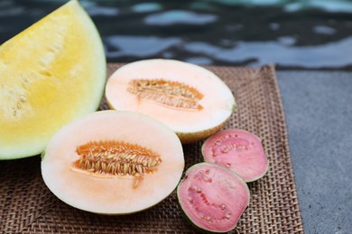 Photo of Ripe juicy tropical fruits on wicker tray near swimming pool, closeup