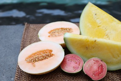 Photo of Ripe juicy tropical fruits on wicker tray near swimming pool, closeup