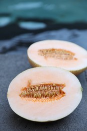 Photo of Halves of juicy melon on grey surface near swimming pool, closeup