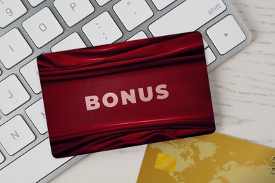 Image of Bonus card with stylish design and computer keyboard on white wooden table, top view