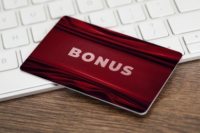 Image of Bonus card with stylish design and computer keyboard on wooden table