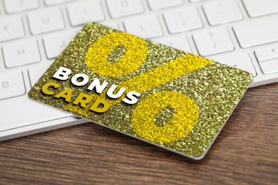 Image of Bonus card with stylish design and computer keyboard on wooden table