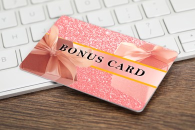 Image of Bonus card with stylish design and computer keyboard on wooden table