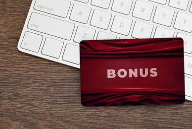 Image of Bonus card with stylish design and computer keyboard on wooden table, top view