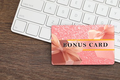 Image of Bonus card with stylish design and computer keyboard on wooden table, top view