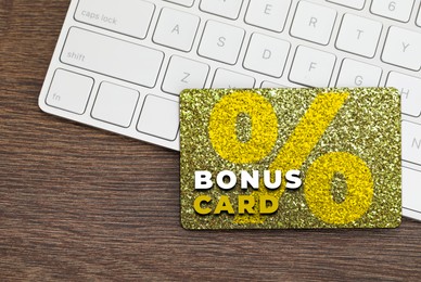 Image of Bonus card with stylish design and computer keyboard on wooden table, top view
