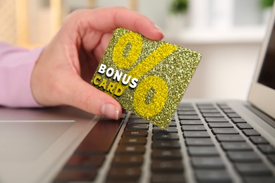 Image of Woman holding Bonus card with stylish design near laptop, closeup