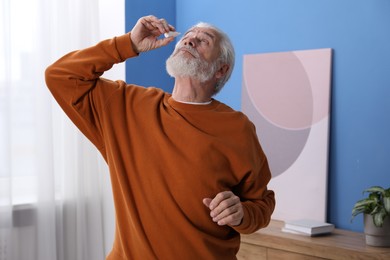 Photo of Senior man applying eye drops at home