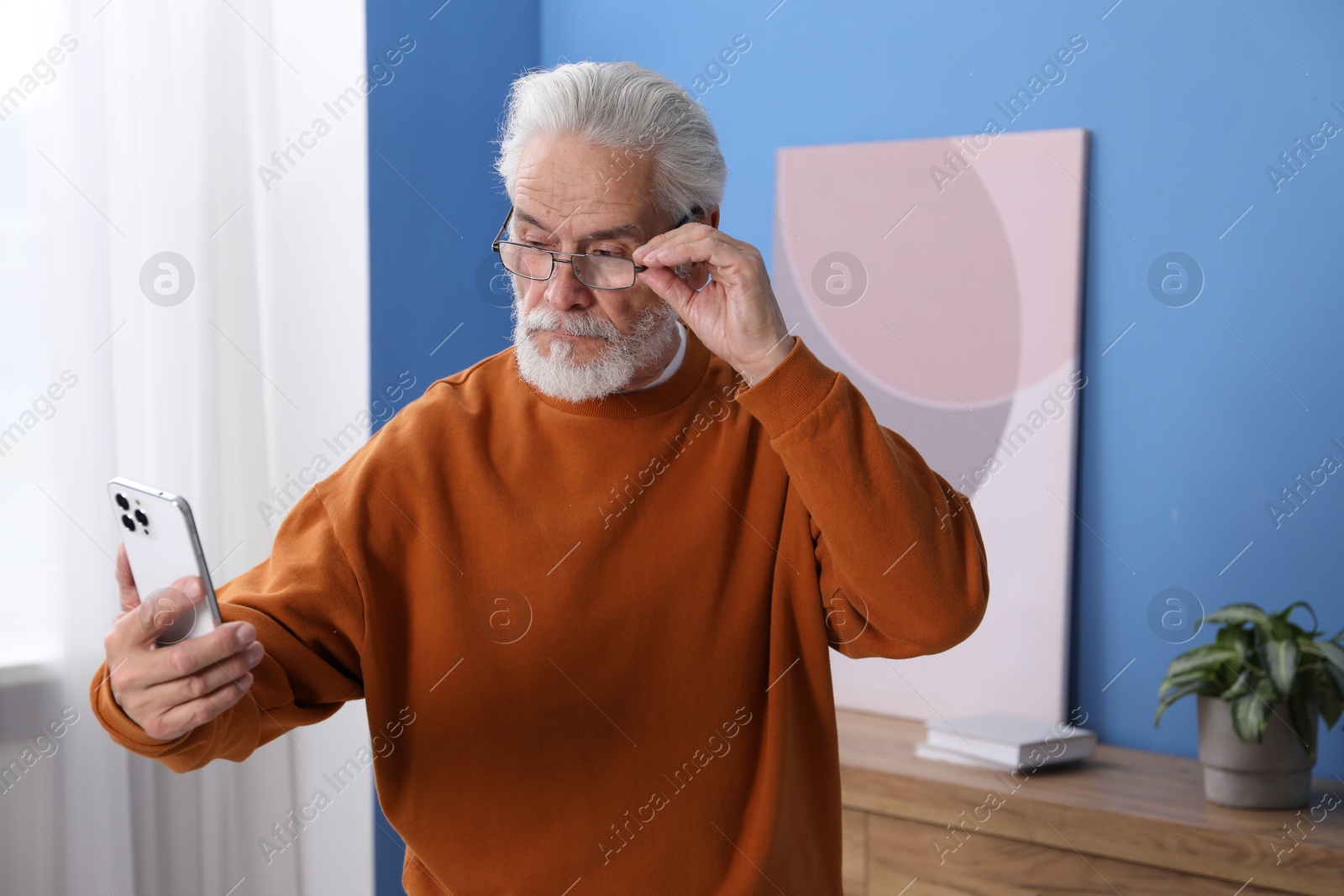Senior man with vision problem using smartphone at home Photo of Senior man with vision problem using smartphone at home