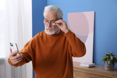 Photo of Senior man with vision problem using smartphone at home