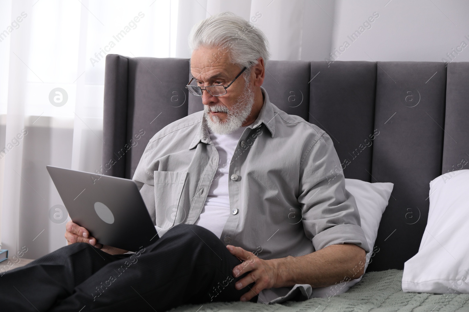 Senior man with vision problem using laptop on bed at home Photo of Senior man with vision problem using laptop on bed at home