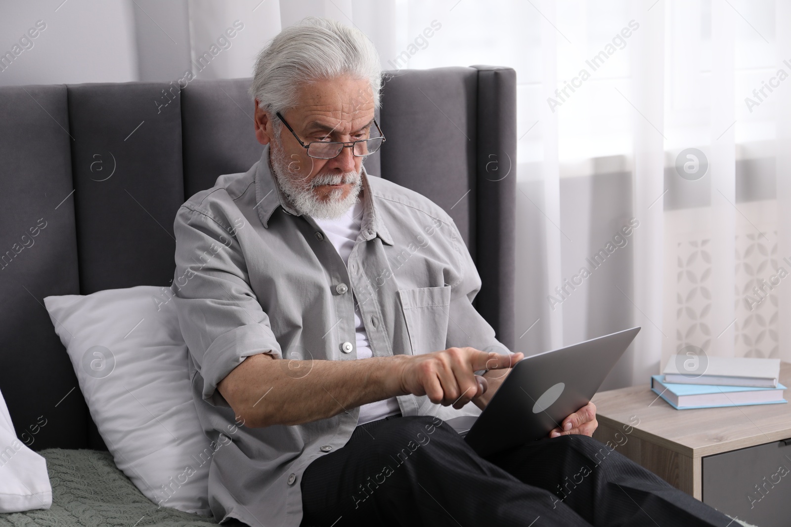 Senior man with vision problem using laptop on bed at home Photo of Senior man with vision problem using laptop on bed at home