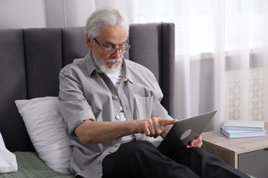 Photo of Senior man with vision problem using laptop on bed at home