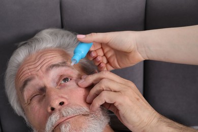 Photo of Woman dripping medication into man's eye at home, closeup