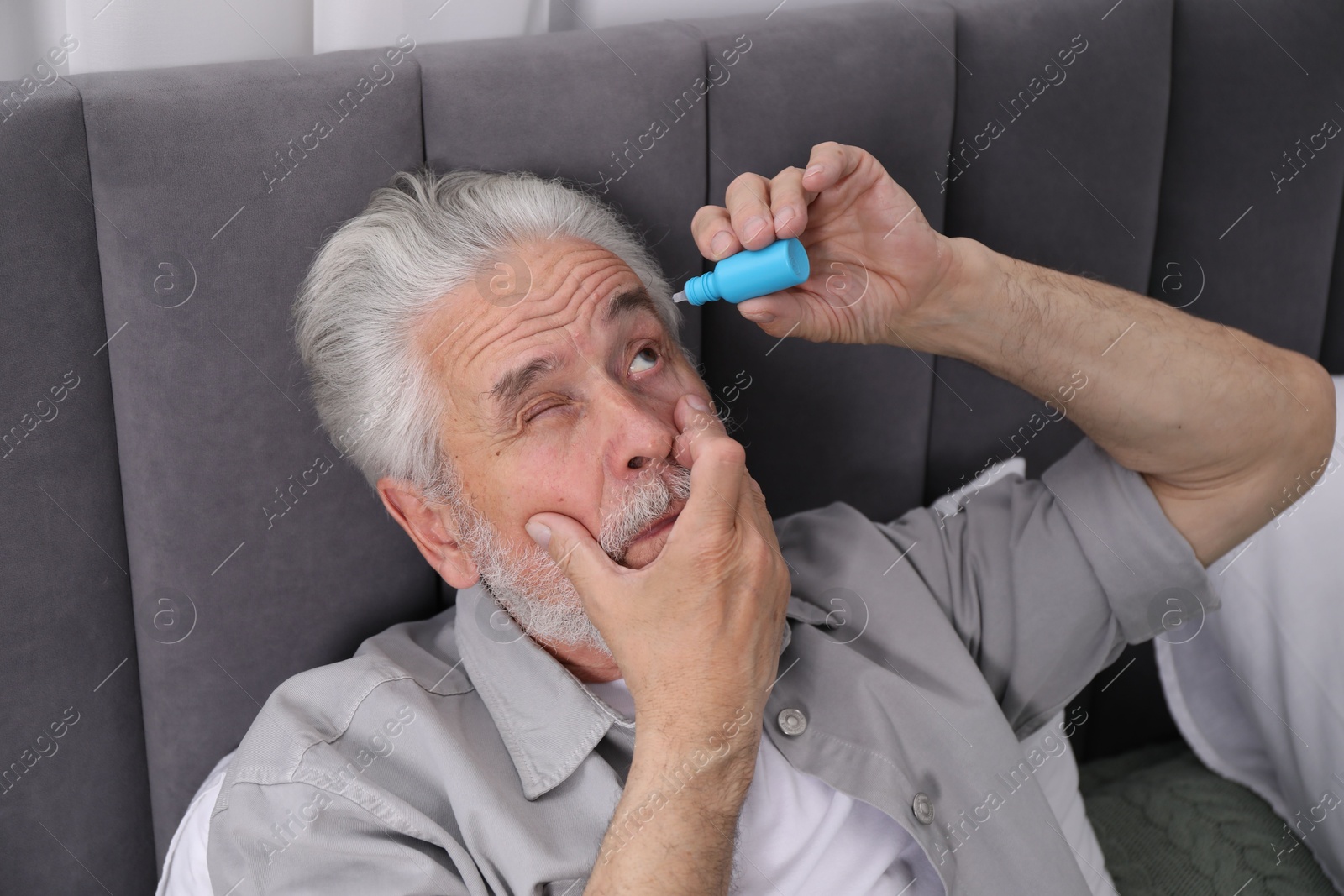 Senior man applying eye drops on bed at home Photo of Senior man applying eye drops on bed at home