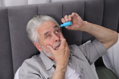 Photo of Senior man applying eye drops on bed at home