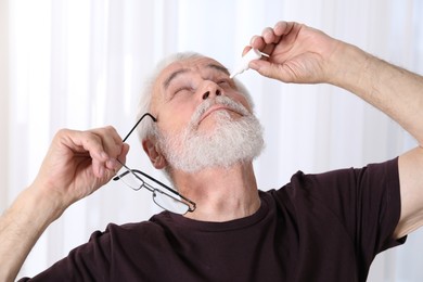 Photo of Senior man applying eye drops at home