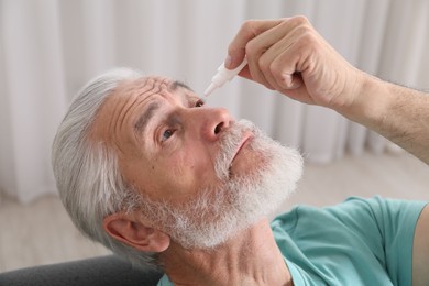 Photo of Senior man applying eye drops at home