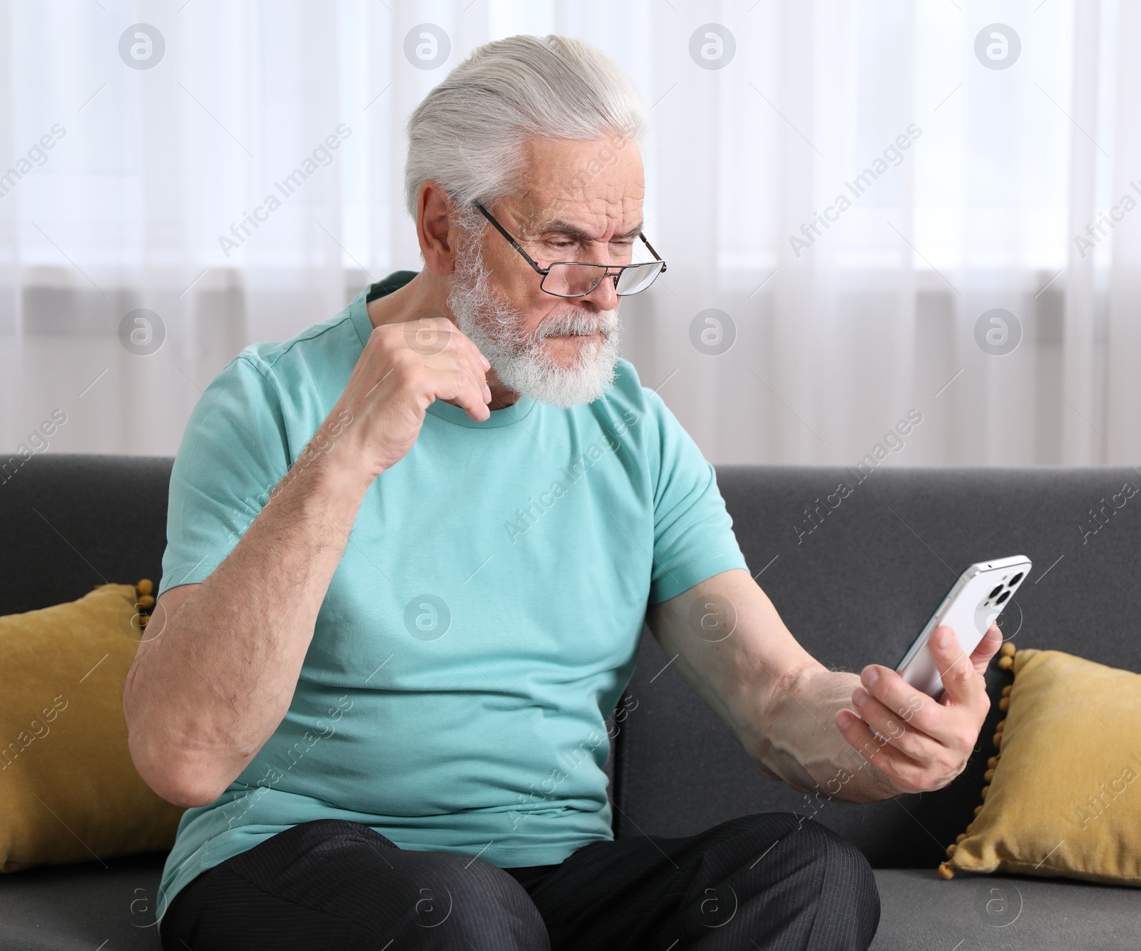 Senior man with vision problem using smartphone on sofa at home Photo of Senior man with vision problem using smartphone on sofa at home