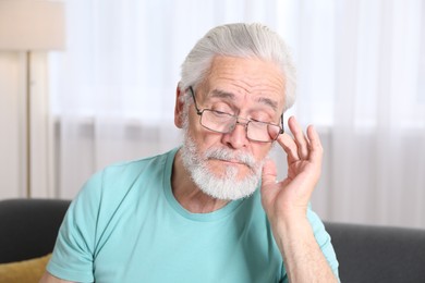 Photo of Senior man in glasses suffering from eyestrain at home