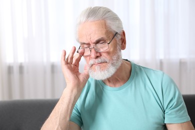 Photo of Senior man in glasses suffering from eyestrain at home