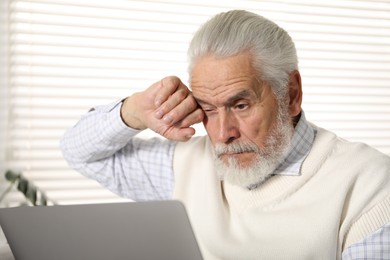 Photo of Senior man with vision problem using laptop at home