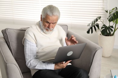 Photo of Senior man with vision problem using laptop in armchair at home