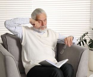Photo of Senior man with glasses suffering from eyestrain in armchair at home