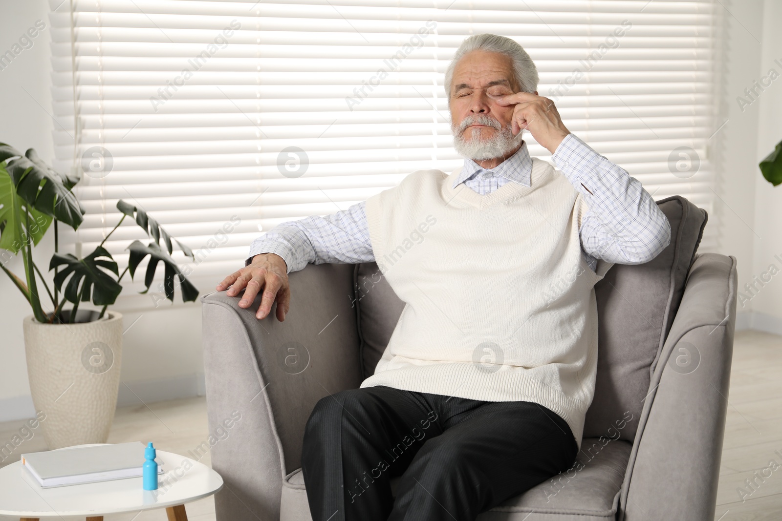 Senior man suffering from eyestrain in armchair at home Photo of Senior man suffering from eyestrain in armchair at home
