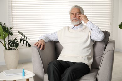 Photo of Senior man suffering from eyestrain in armchair at home