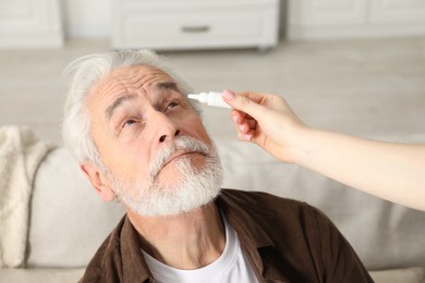 Photo of Woman dripping medication into man's eye at home, closeup