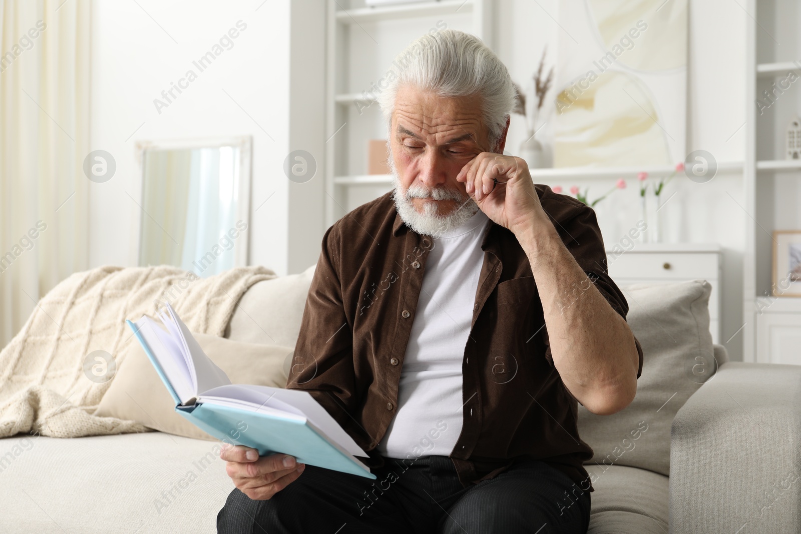 Senior man with vision problem reading book on sofa at home Photo of Senior man with vision problem reading book on sofa at home