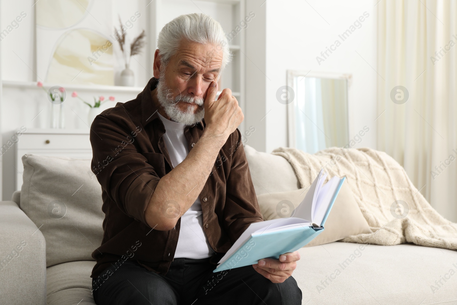 Photo of Senior man with vision problem reading book on sofa at home, space for text